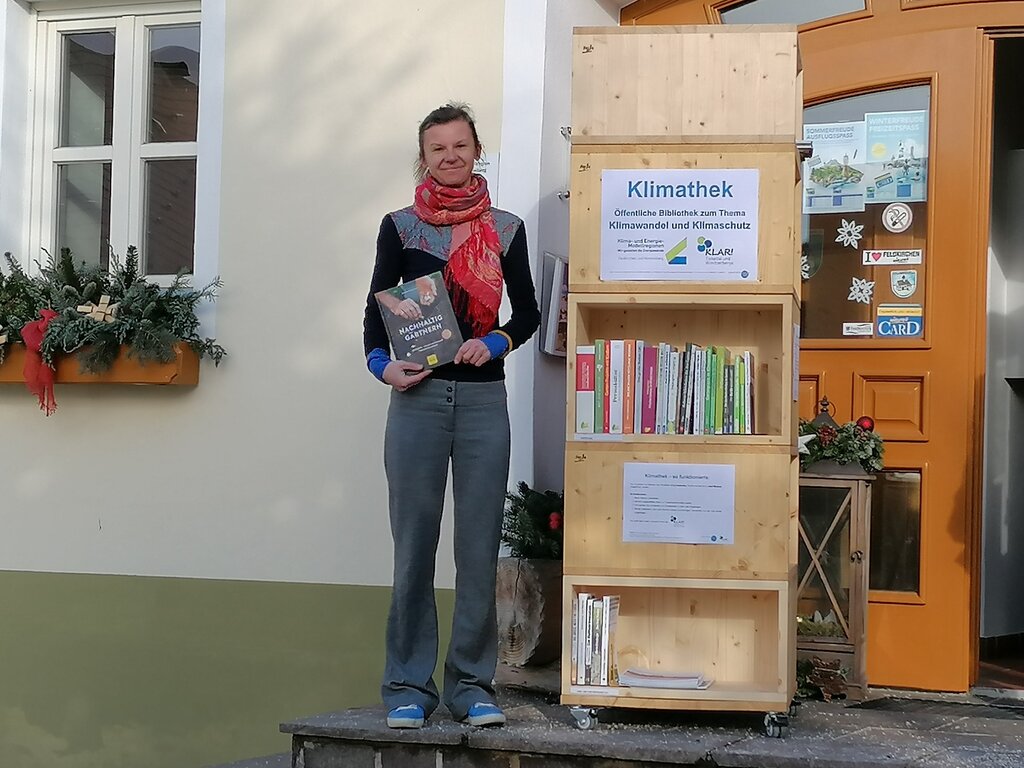 Klimathek mit Büchern und links davon Frau mit Buch in der Hand.