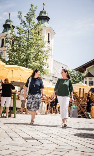 Zwei Frauen auf einem Marktplatz mit einer Kirche im Hintergrund