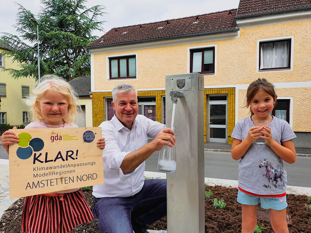 Zwei Mädchen freuen sich mit Landtagsabgeordnetem und Bürgermeister Anton Kasser über den neuen Trinkbrunnen am Kröllendorfer Ortsplatzfer Ortsplatz!